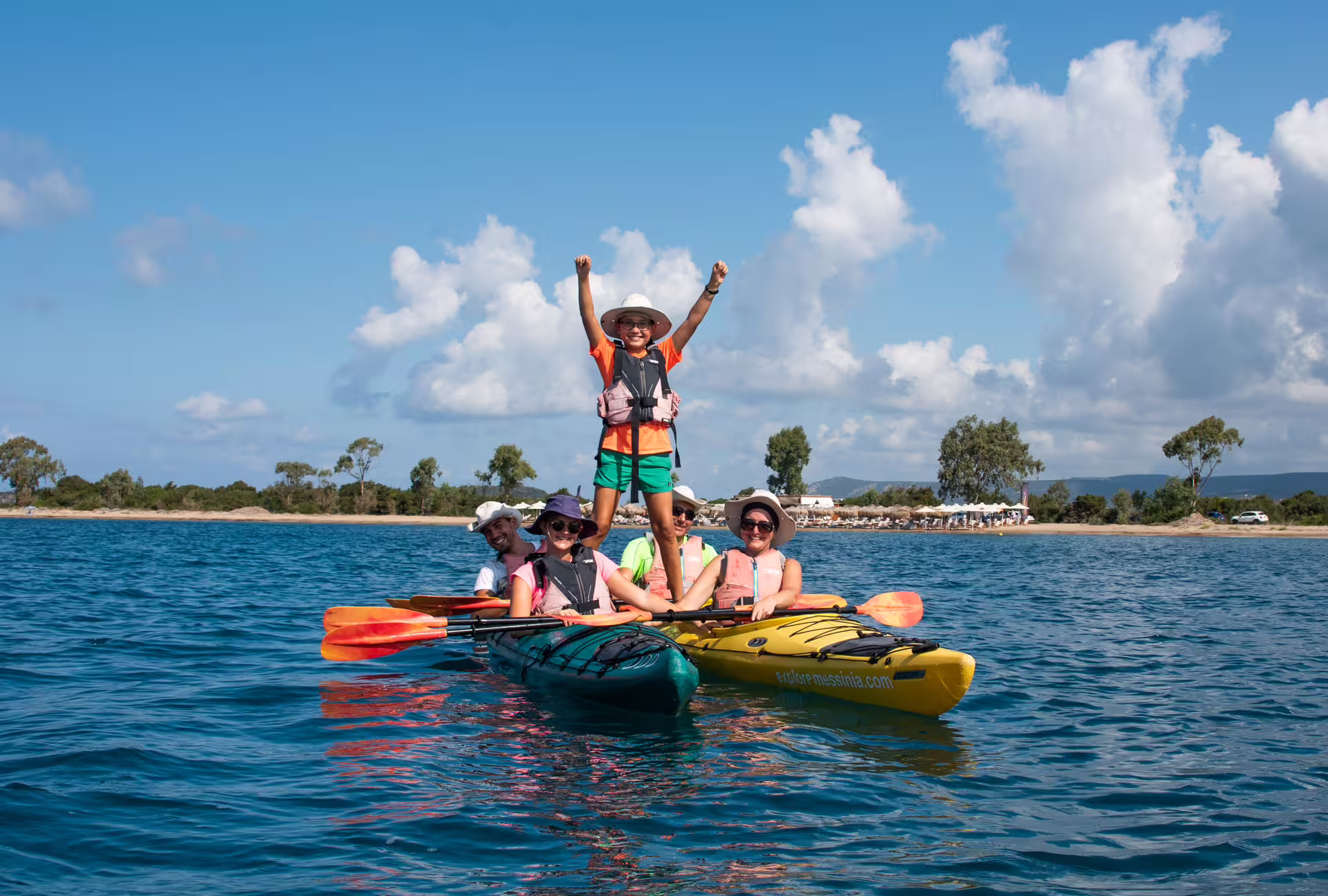 Group sea kayaking in Navarino Bay, Messinia, with tandem kayaks and beach backdrop on a sunny day