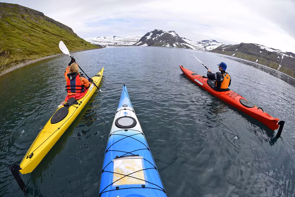 Sea kayaking with guides on a mountain fjord lake, Paddle in the Wild tour with snowcapped peaks ahead