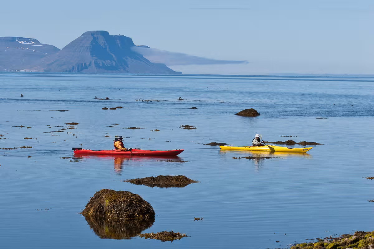 Sea kayaking on calm coastal waters during Solar Eclipse Wild Camp Discovery, with mountains on the horizon