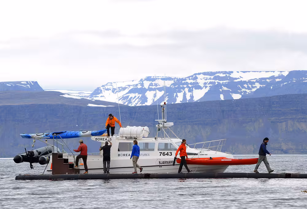Support boat loads sea kayaks at fjord dock with snowy mountains, Paddle in the Wild guided expedition