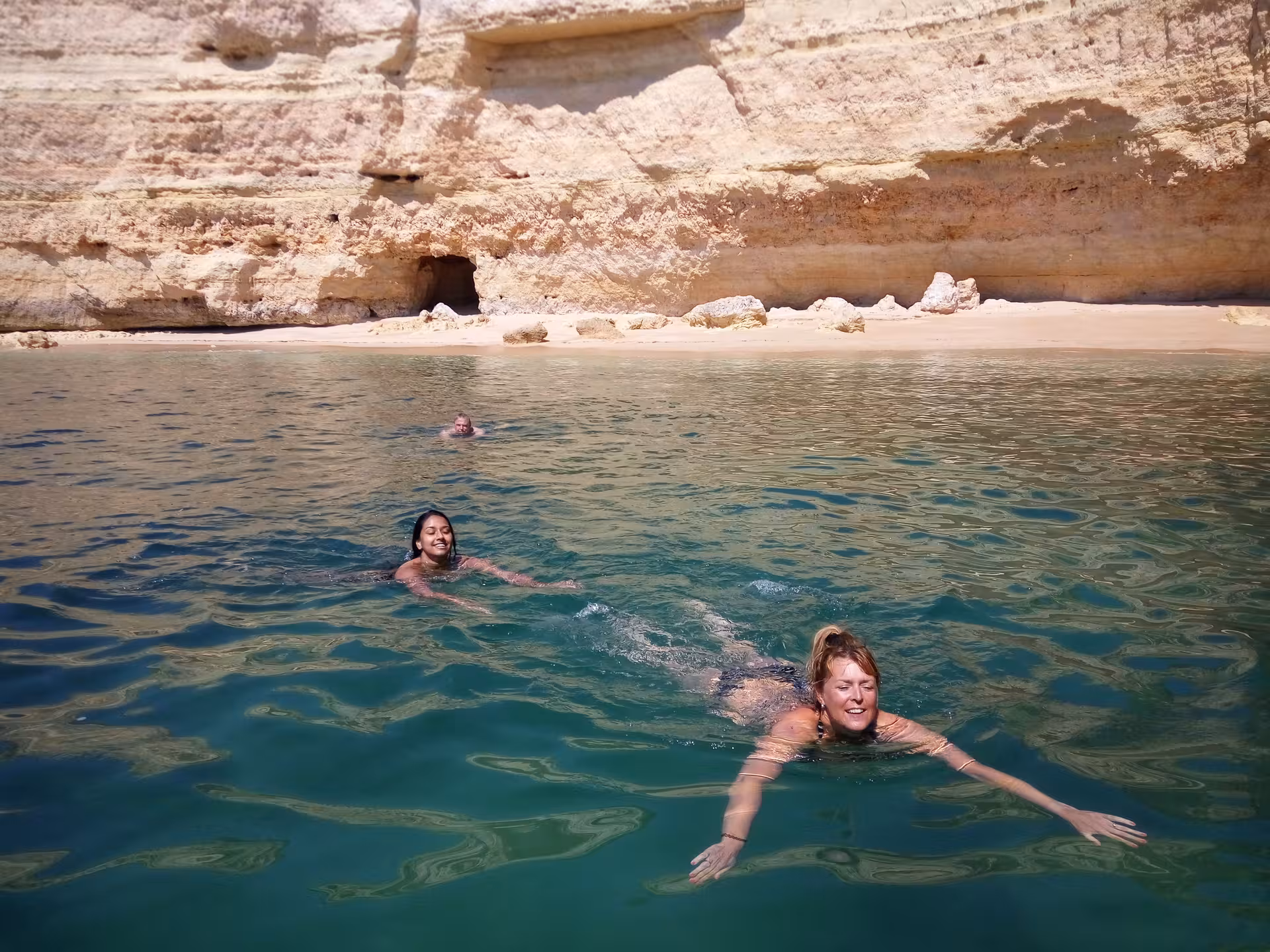 Smiling friends swimming in clear Atlantic waters by golden Algarve cliffs on a private Seasiren Portimão boat tour