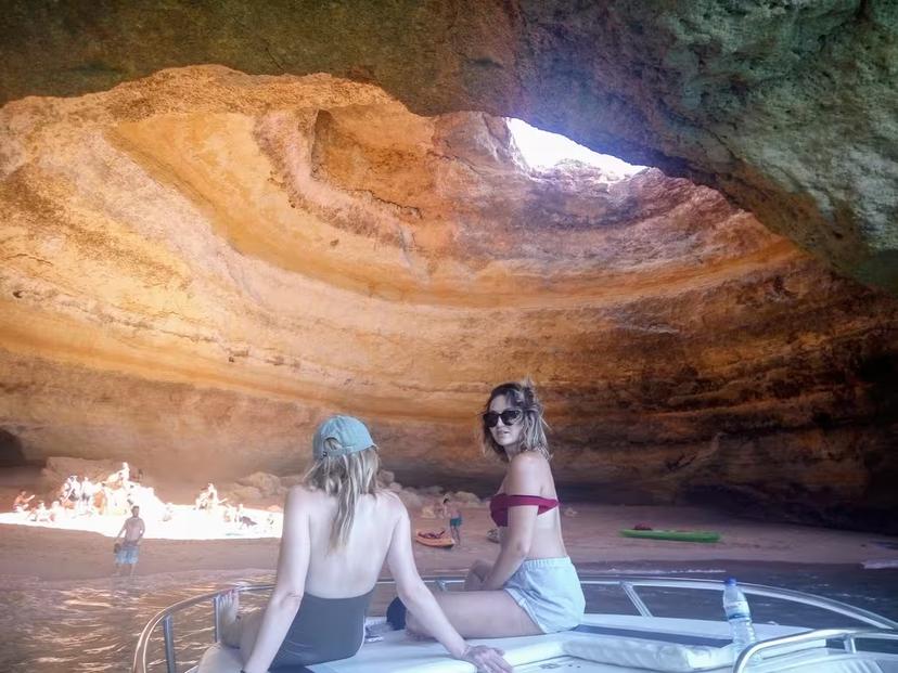 Two women relax on a boat inside Benagil Cave on the Seasiren Private Tour 2H, admiring sunlit rock formations and beach