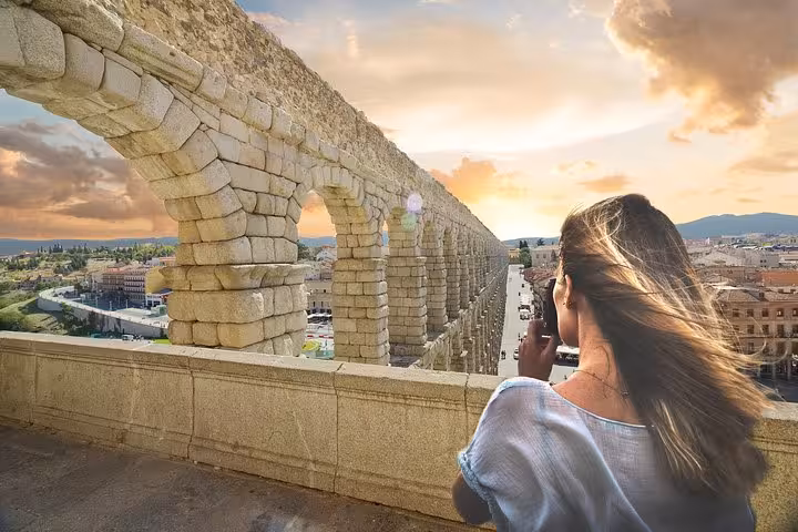 Tourist capturing the majestic Segovia Aqueduct at sunset, a highlight of the Madrid day tour.