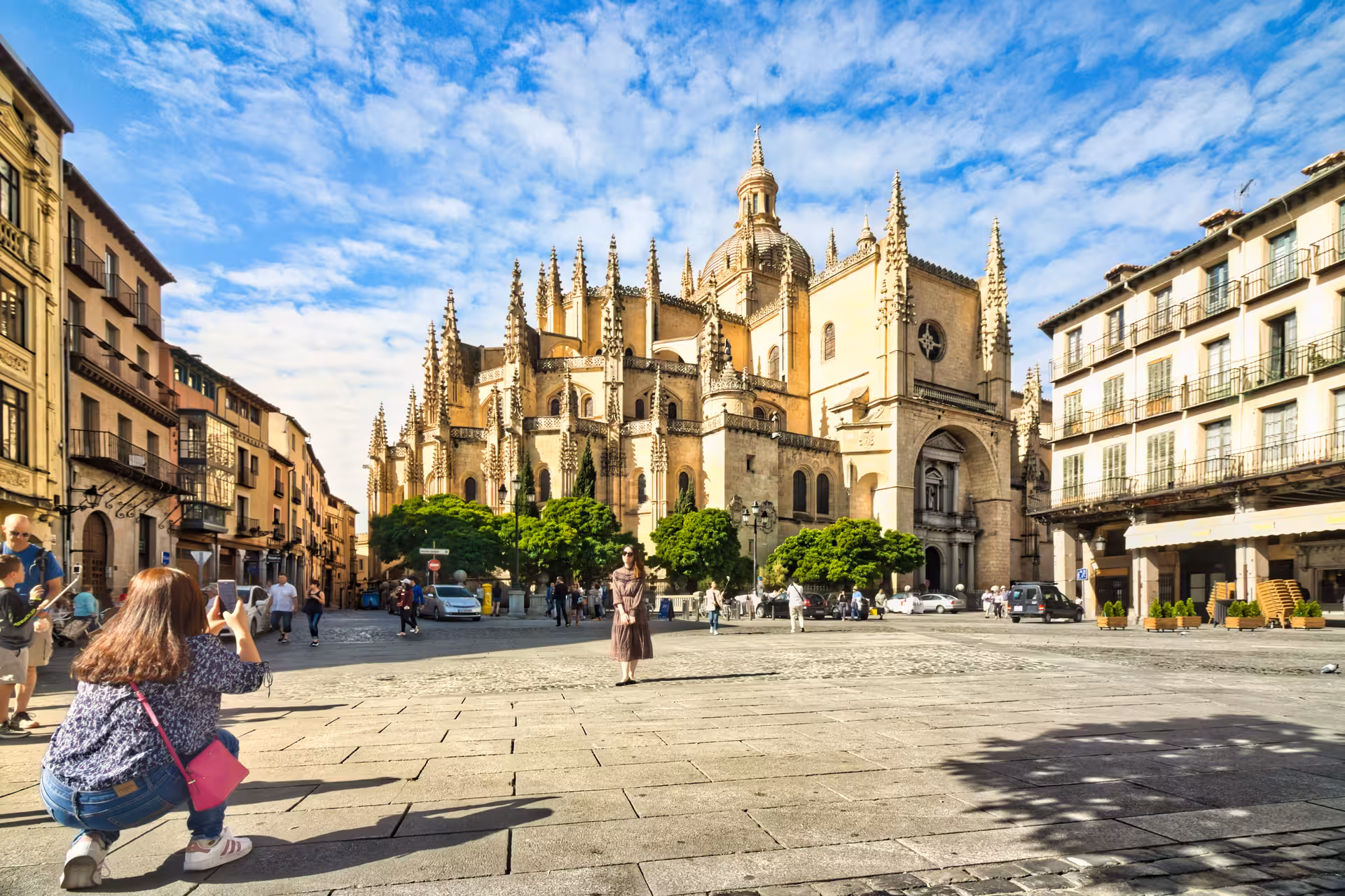 Tourists admire the stunning Segovia Cathedral under a bright blue sky during a day trip from Madrid.