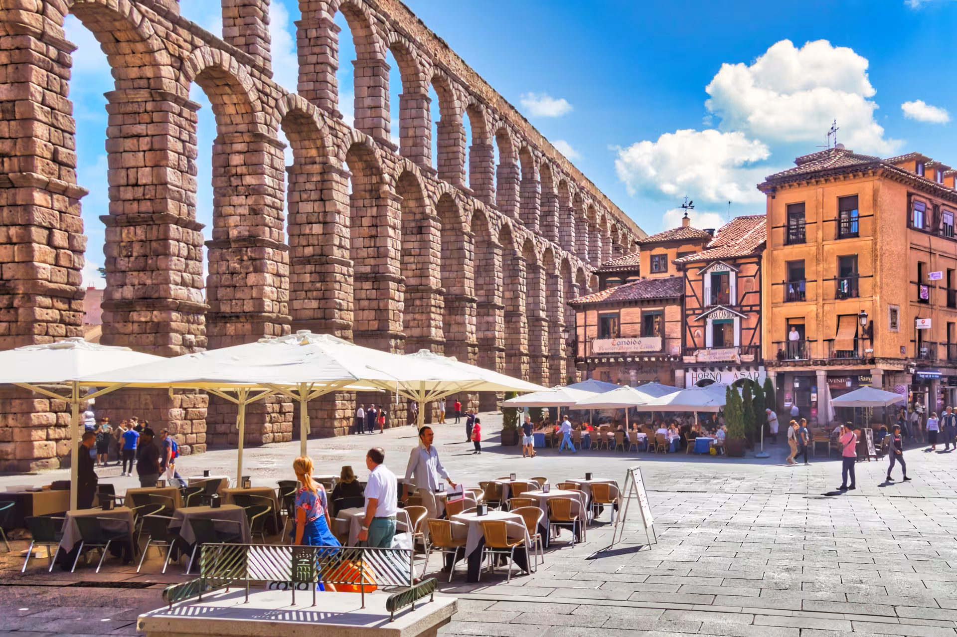 Café patrons enjoy views of the historic Roman aqueduct in Segovia, a highlight of the full day trip from Madrid.