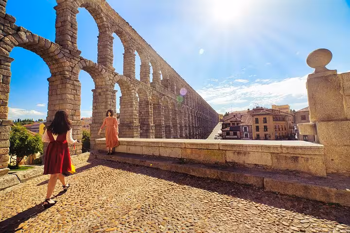 Visitors explore the iconic Roman aqueduct in Segovia, basking in the sunlight during a guided tour of historic sites.
