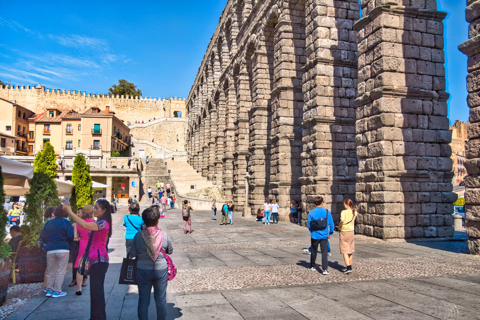 Tourists explore the historic Roman aqueduct in Segovia on a sunny day, ideal for a day trip from Madrid.