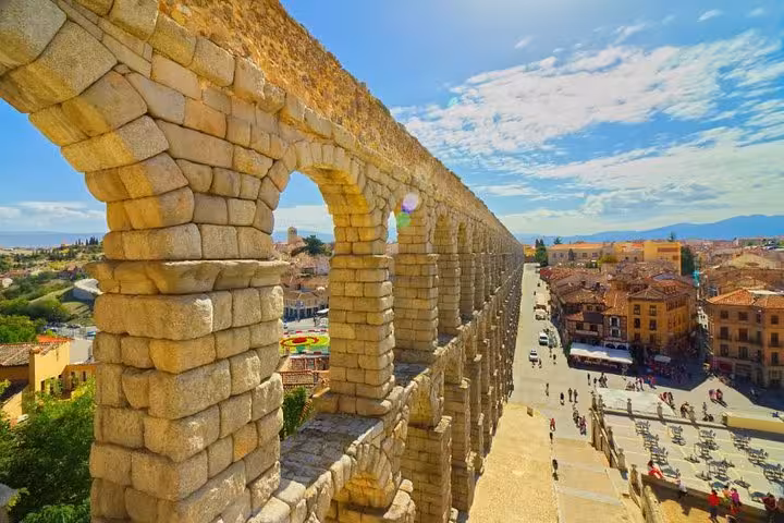 Close-up of Segovia's Roman aqueduct with its towering arches and a vibrant cityscape in the background.