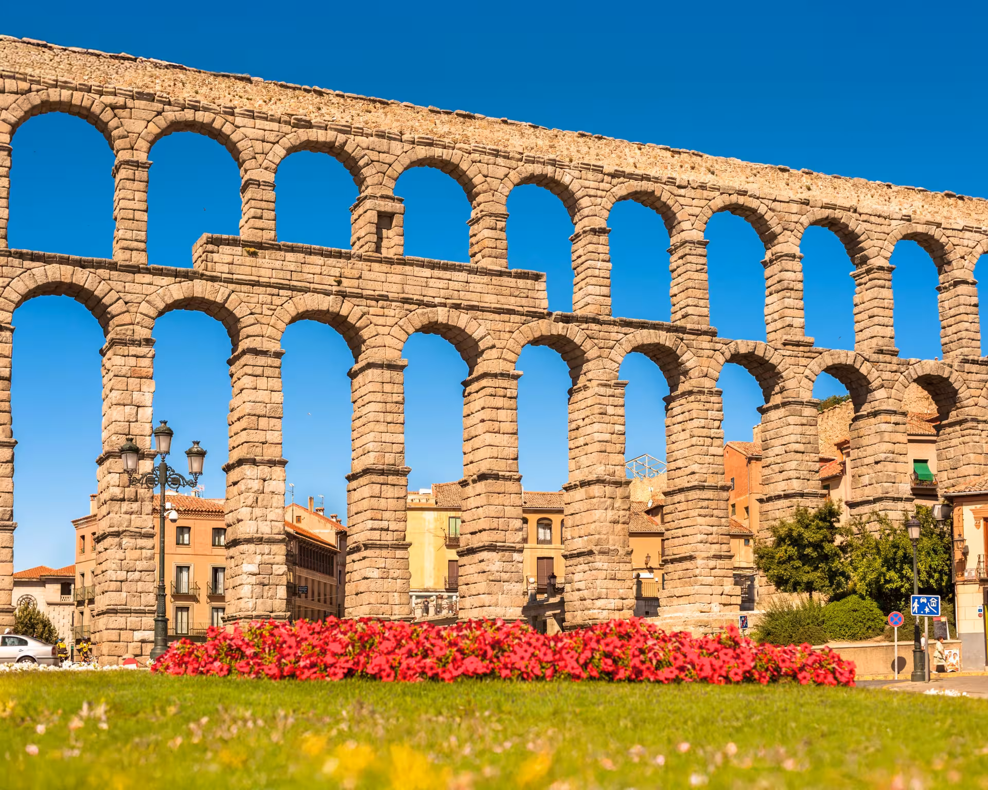 Close-up of Segovia's iconic Roman aqueduct with vibrant red flowers and a clear blue sky, ideal for sightseeing.
