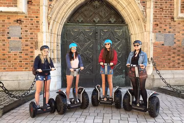 Four tourists on Segways pose in front of a historic building during a 120 min Old Town Segway Tour in Krakow.