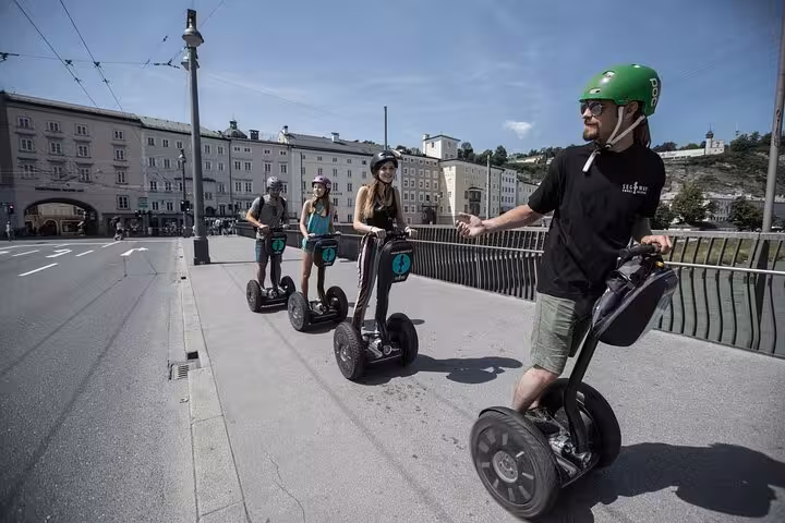Group enjoying a guided Segway tour crossing a bridge in Salzburg with scenic views of historic architecture.