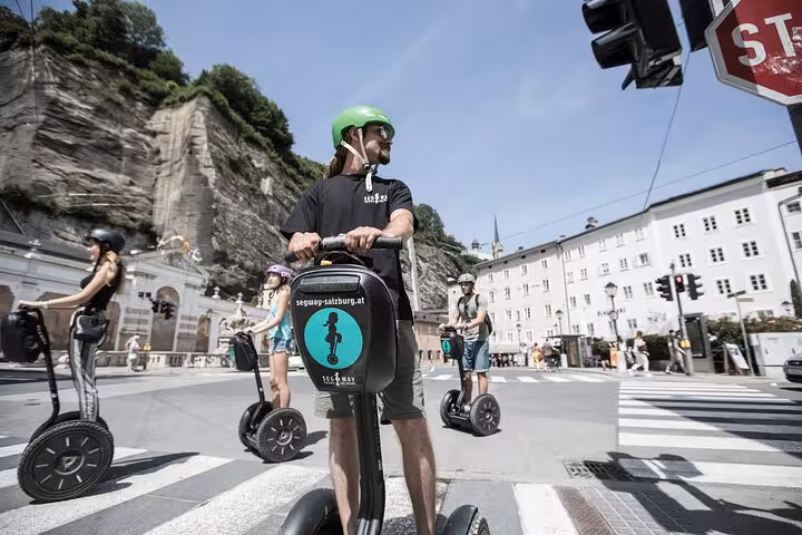Tour guide leading a Segway group through a Salzburg intersection, surrounded by historic buildings and cliffs.