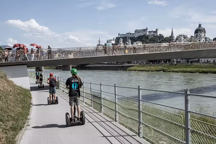 Segway riders explore the riverside path with views of Salzburg's iconic architecture and bridges.