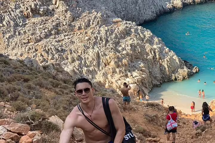 Tourist hiking down to the secluded Seitan Limania Beach, Crete, with rocky cliffs and vibrant blue sea in the background.