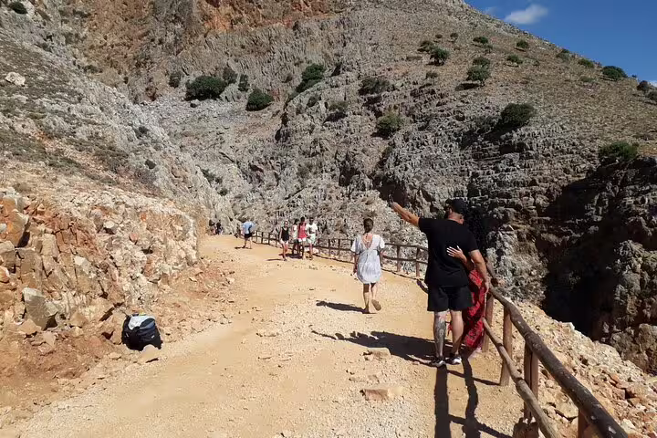 Tourists walking along a rugged path with breathtaking views at Seitan Limania, capturing the essence of a coastal adventure.