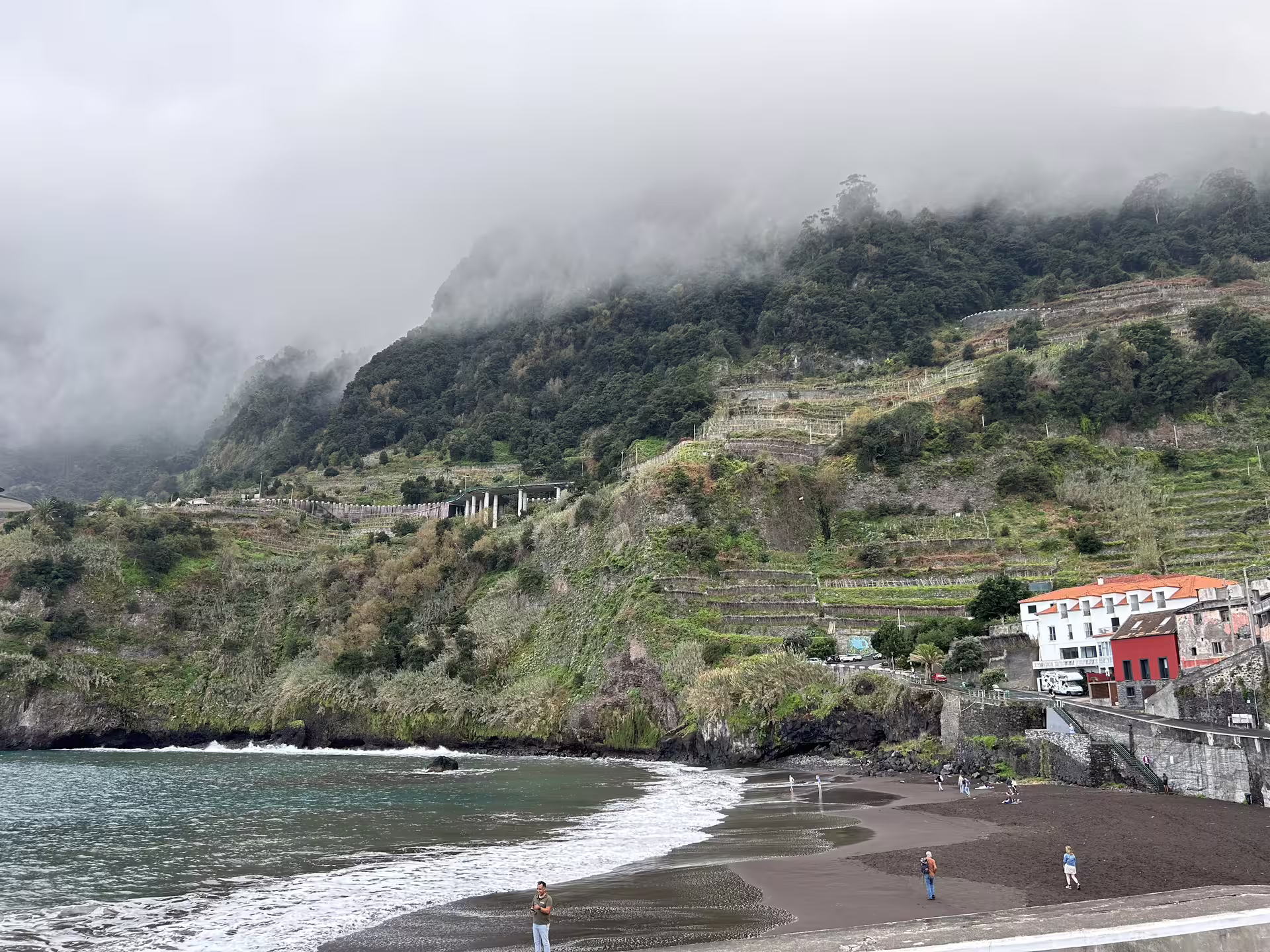 Scenic view of Seixal beach with lush terraced hills and misty clouds, featured in the Cabo Girão full-day tour.