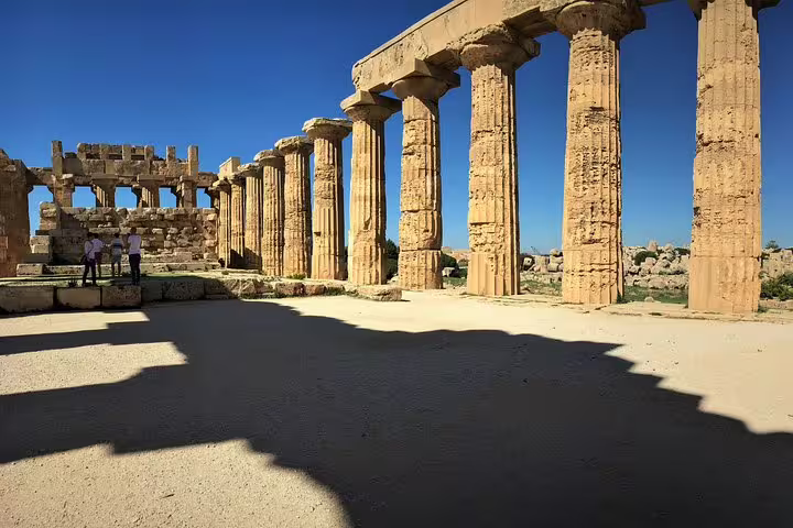 Visitors explore the sunlit Doric columns of Tempio E at Selinunte Archaeological Park during a private tour from Palermo