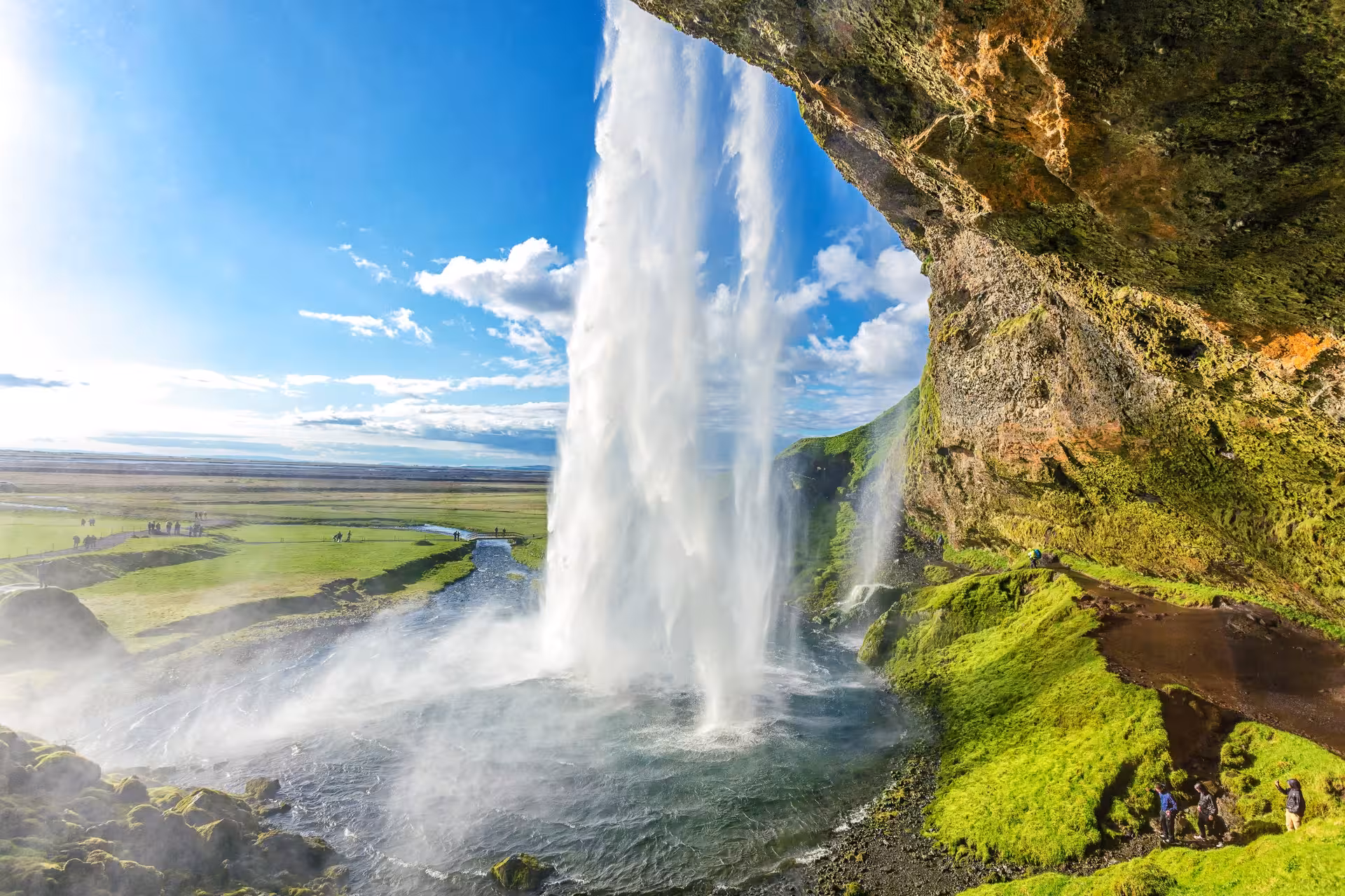 Seljalandsfoss waterfall cascading over mossy cliffs under a bright blue sky, a highlight of Iceland's scenic road trip.