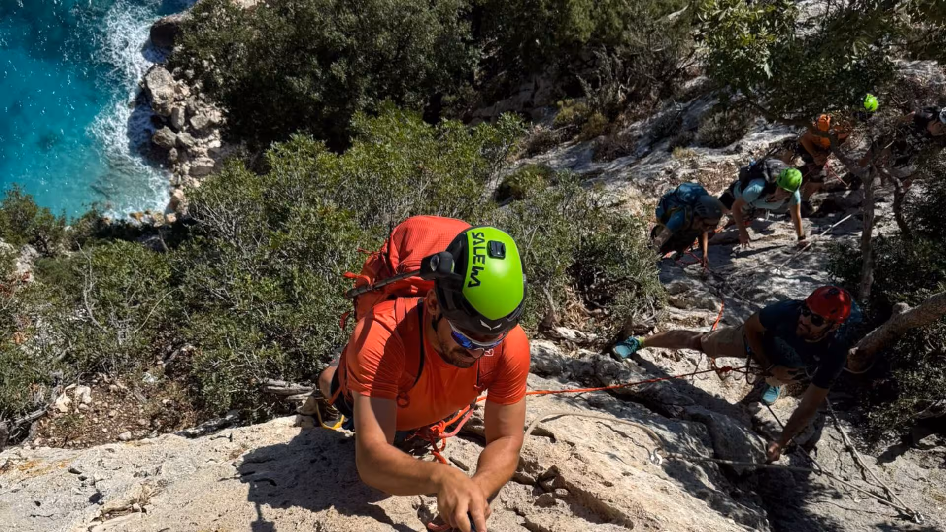 Adventurer climbing rocky terrain on Selvaggio Blu trek with turquoise sea in the background.