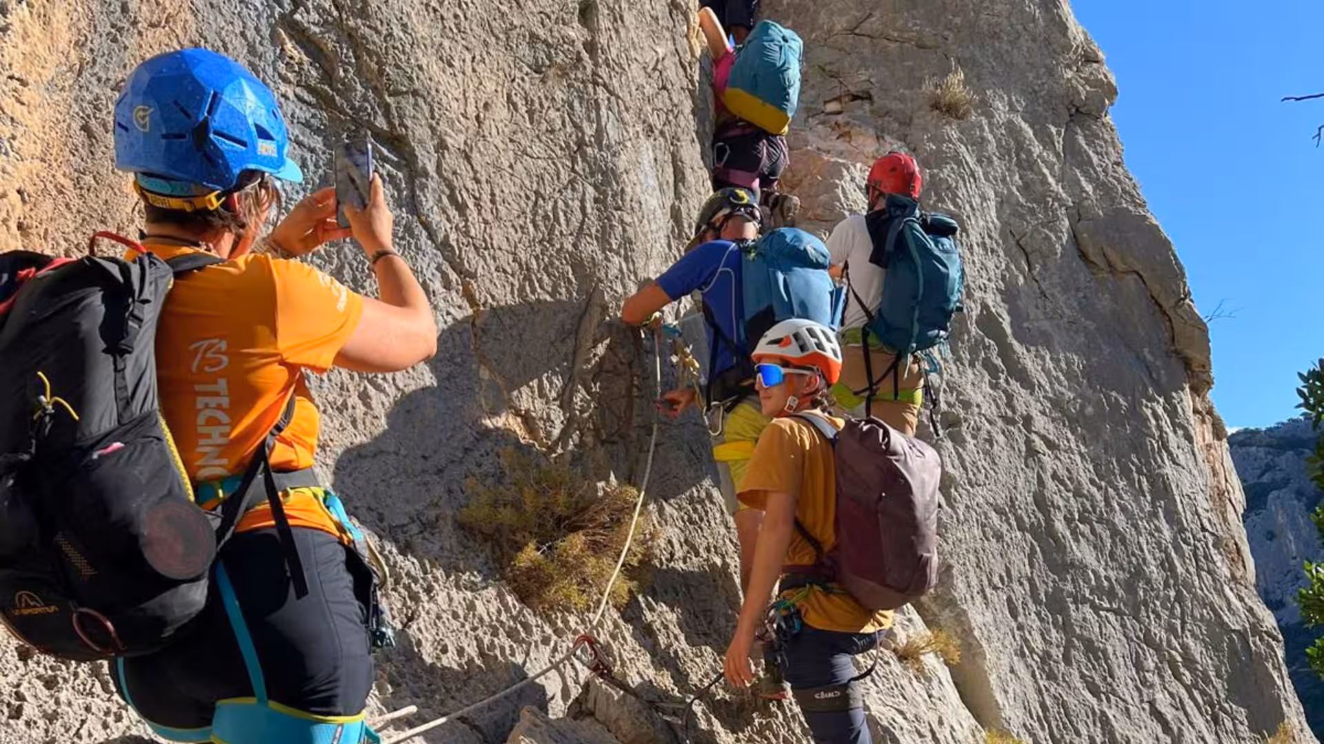 Group of trekkers climbing a rocky path on the Selvaggio Blu route in Sardinia with safety gear.