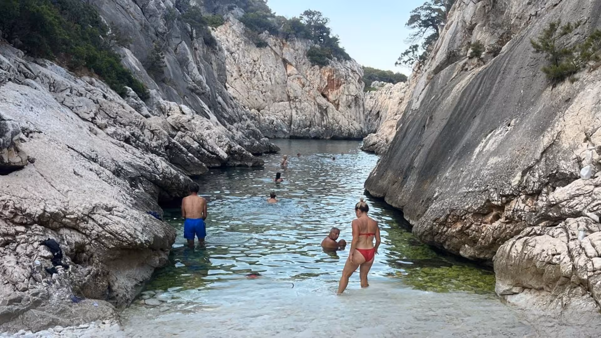 Swimmers enjoying the clear waters surrounded by rocky cliffs on the Selvaggio Blu trekking tour from Arbatax.
