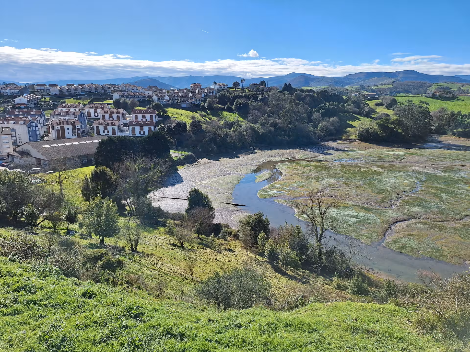 Panoramic view of lush landscape and river near San Vicente de la Barquera on a sunny day.