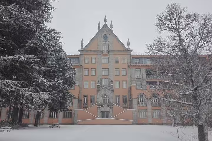 Snow-covered historic building in Serra da Estrela, Portugal, surrounded by trees, featured on a private tour from Lisbon.
