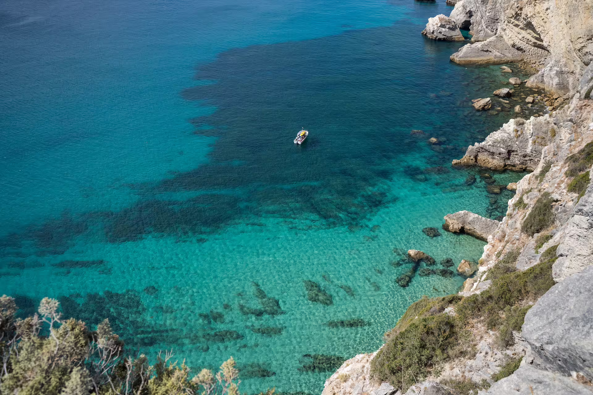 Aerial view of a small boat on the crystal-clear turquoise waters near rocky cliffs in Sesimbra, Arrábida Park, Portugal.