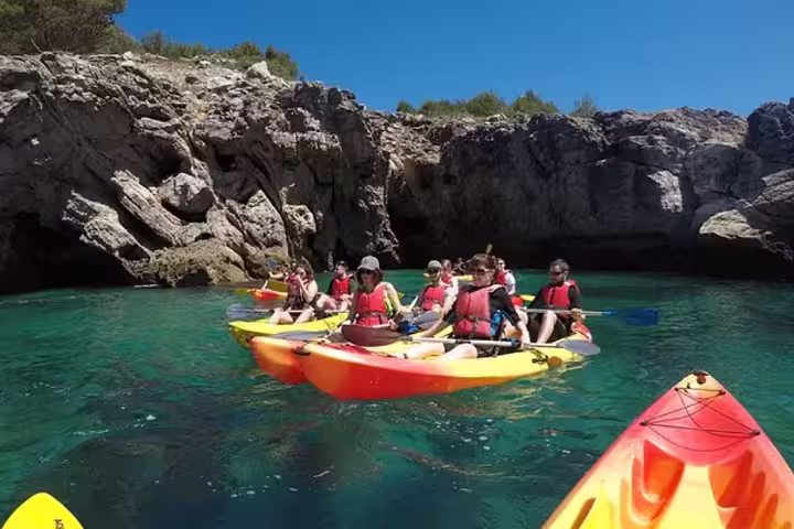 Kayakers explore crystal-clear waters and rocky cliffs on a small group tour in Sesimbra's Arrábida Natural Park.