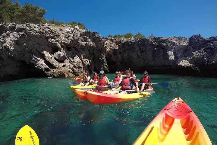 Kayakers explore crystal-clear waters and rocky cliffs on a small group tour in Sesimbra, Arrábida Natural Park.
