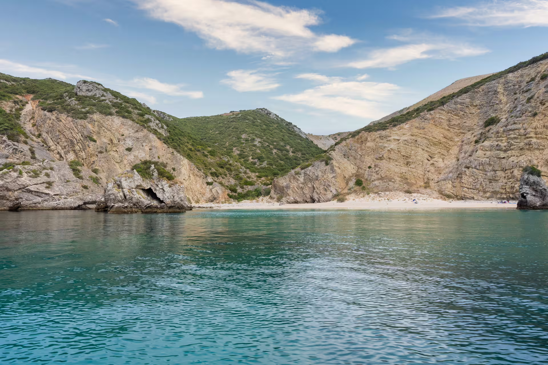 Scenic view of a secluded beach and rocky cliffs in Sesimbra's Arrábida Park, captured during a private boat tour.