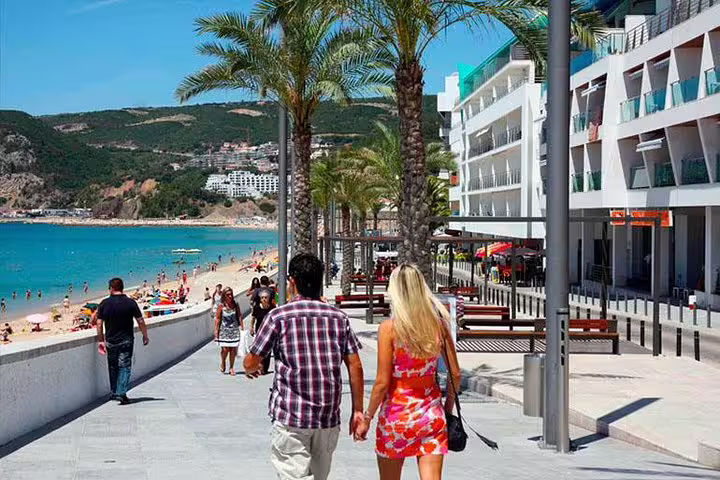 Visitors strolling along the beachfront promenade in Sesimbra, enjoying views of the ocean and palm-lined walkways.