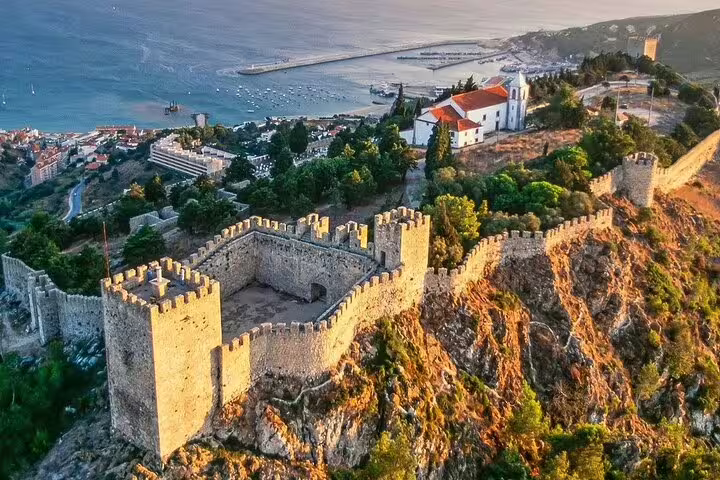 Aerial view of Sesimbra Castle overlooking the coastline, featuring lush landscapes and historic architecture on an Arrábida day trip.