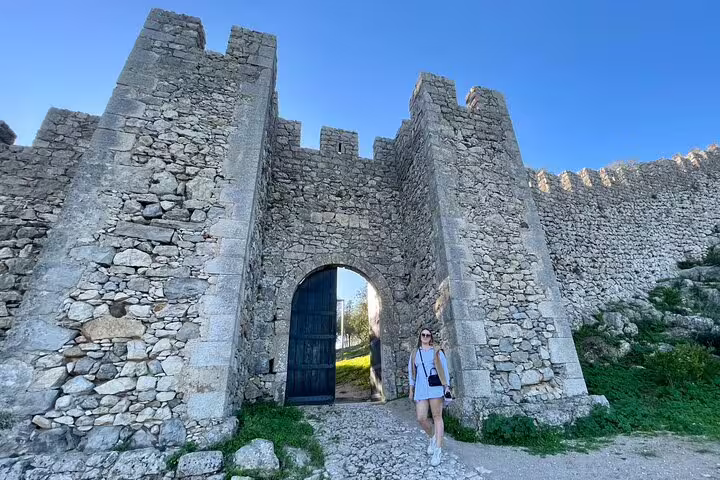 Visitor explores the historic stone gateway of Sesimbra Castle, a highlight of the Azeitão cheese and wine tasting tour.