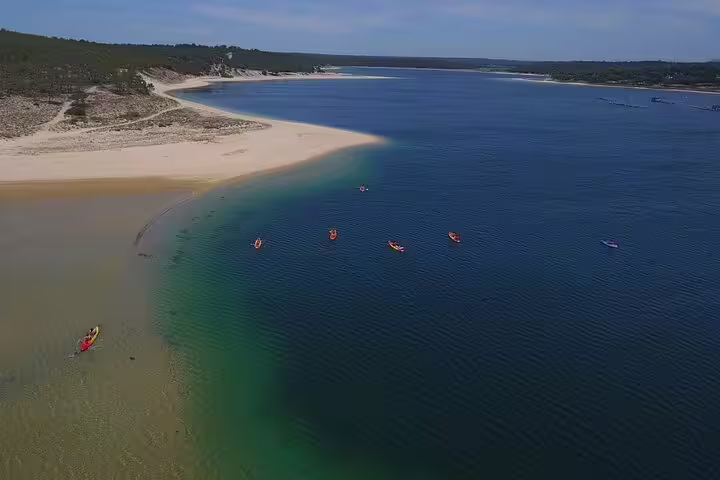 Aerial view of kayakers enjoying a tranquil paddle in the crystal-clear waters of Sesimbra's scenic lagoon, surrounded by sandy beaches.