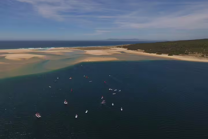 Aerial view of kayakers exploring the serene, turquoise waters of a picturesque lagoon near Sesimbra under a clear blue sky.