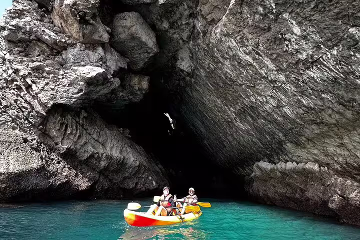 Kayakers explore a stunning rocky cave on a small group tour in Sesimbra's Arrábida Natural Park, Portugal's coastal gem.