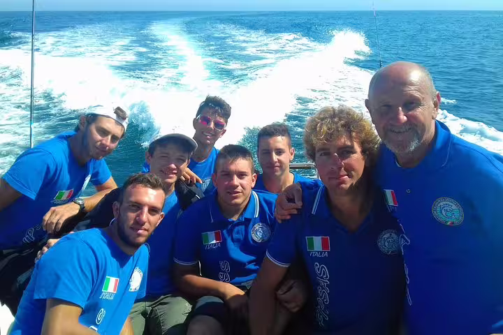 A group of people wearing blue shirts enjoy a sport fishing tour on a boat in Sesimbra, with ocean waves in the background.