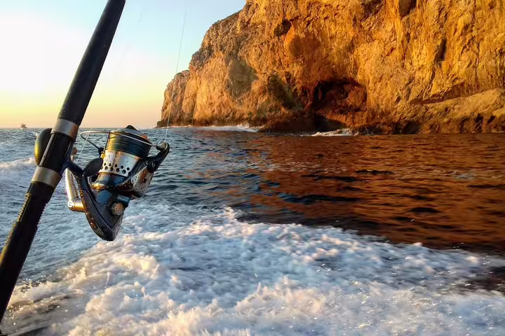 Fishing rod over ocean waves with picturesque rocky cliffs at sunset on an all-inclusive sport fishing tour in Sesimbra.