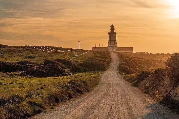 Sunset view of a coastal path leading to a lighthouse in Setúbal, showcasing serene natural beauty and rugged landscapes.