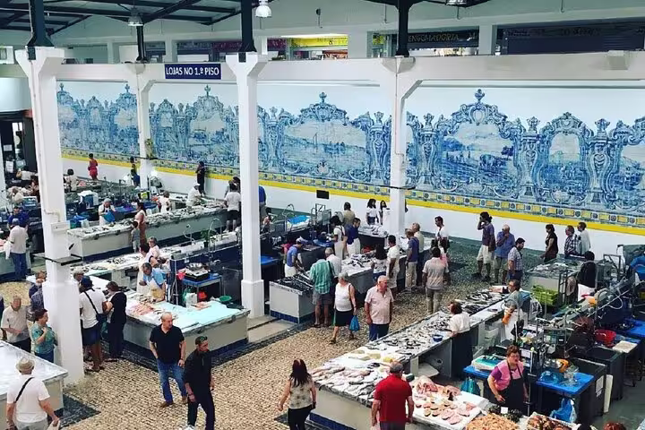 Visitors explore a bustling indoor market with traditional blue tiles in Setúbal, featured in the Arrábida and Azeitão tour.