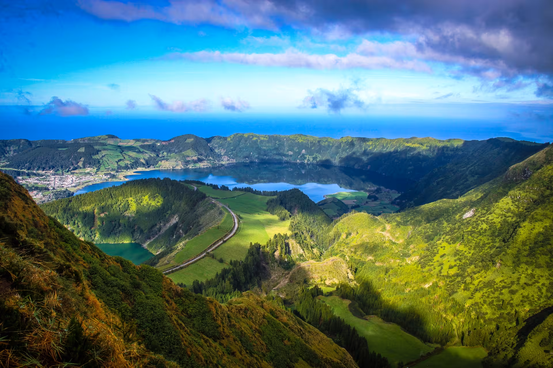 Panoramic view of Sete Cidades crater lakes from Azores hike, green ridges leading to Ferraria coast