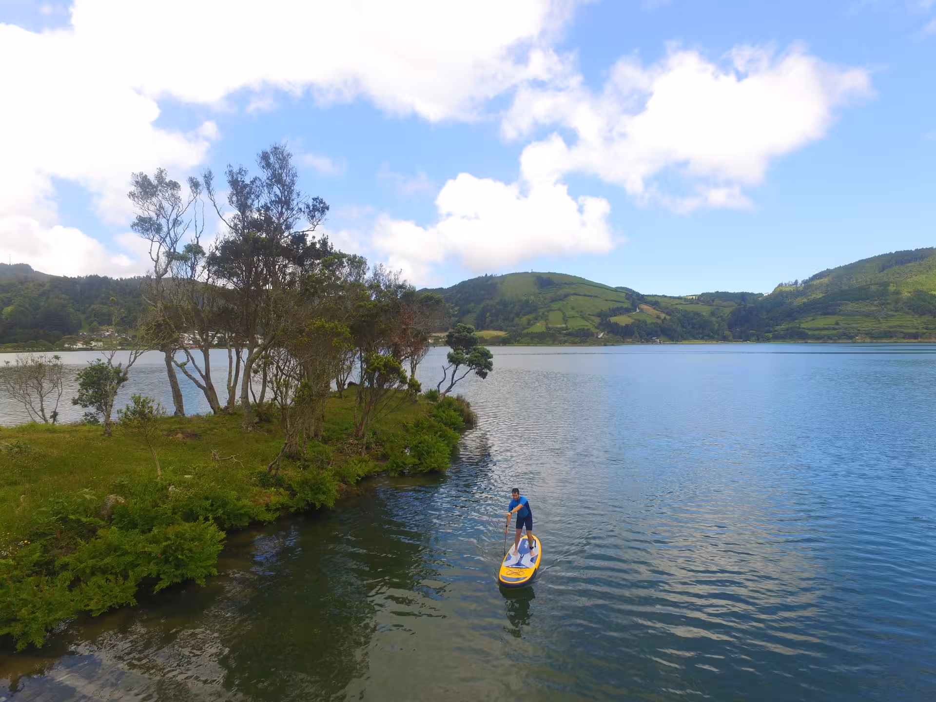 Traveler paddleboarding on Sete Cidades lagoon beside lush green islet, enjoying Azores Seven Cities Experience adventure