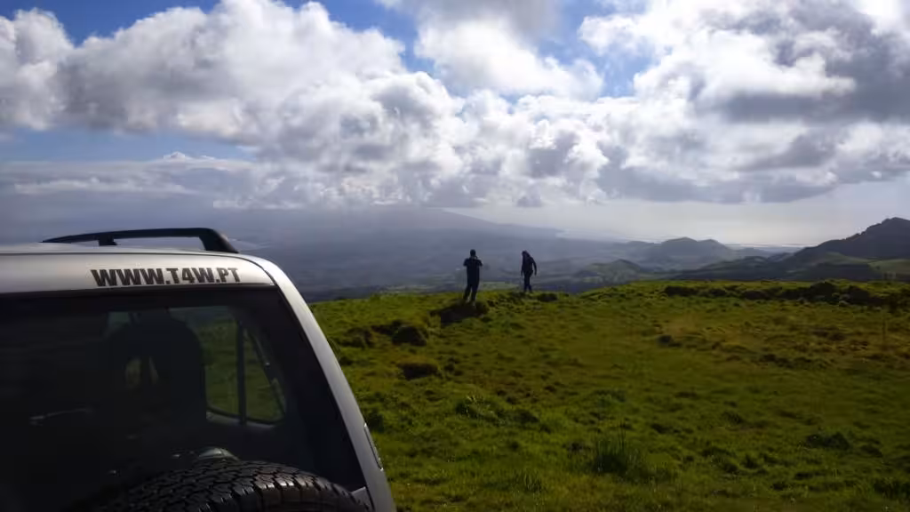 Travelers on a Sete Cidades shore excursion step from a 4x4 to admire sweeping Atlantic and crater views from a grassy ridge