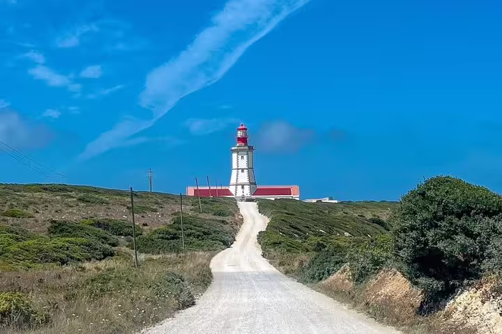 Bright day at a coastal trail leading to a red-roofed lighthouse in Setúbal, emphasizing the region's scenic maritime charm.