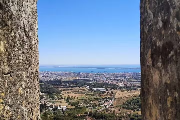 Scenic view of Setúbal's coastline and cityscape framed by ancient castle walls under a clear blue sky.