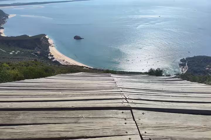 Panoramic vista from a wooden platform overlooking Setúbal's coastline, showcasing stunning beaches and crystal waters.