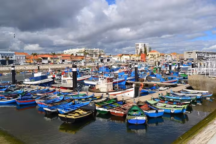 Colorful fishing boats docked in the vibrant Setúbal harbor, with charming buildings and a cloudy sky in the background.