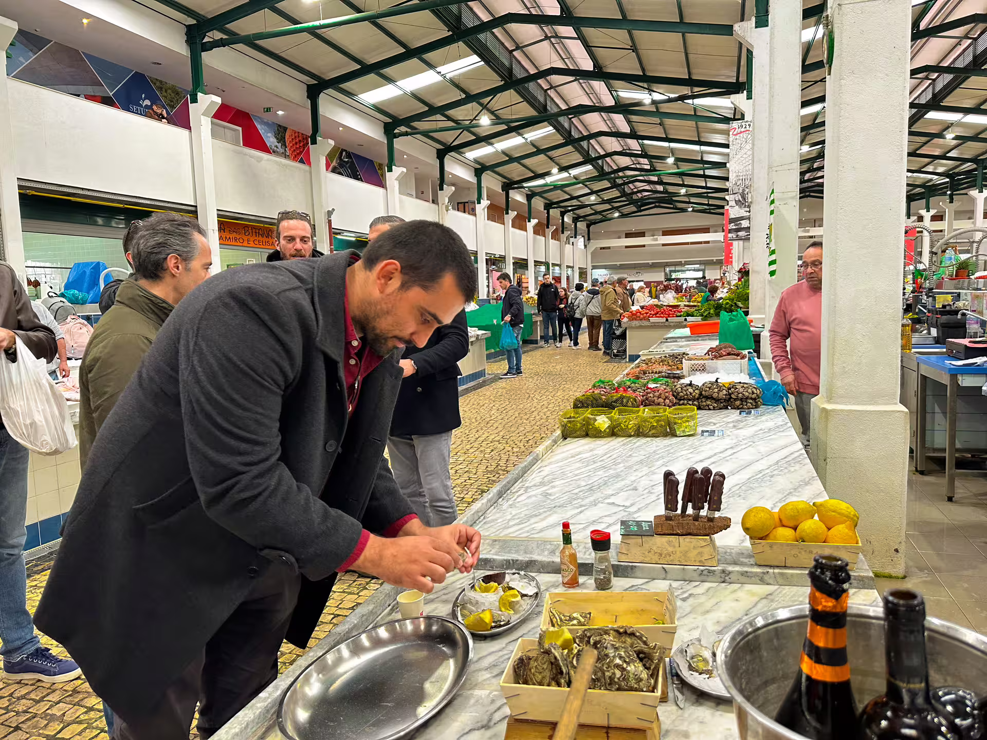 Man preparing seafood at a bustling Setúbal market with fresh produce and local delicacies on display.