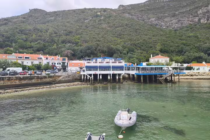 Charming waterfront village in Setúbal with colorful buildings and boats, surrounded by lush green hills and serene waters.